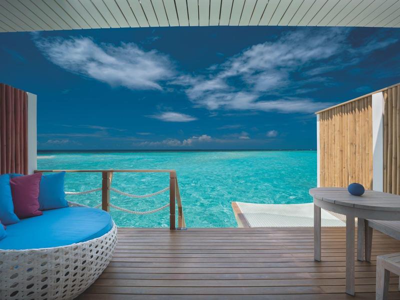 Terraza con sillón y mesa frente a un mar turquesa bajo un cielo azul con nubes.