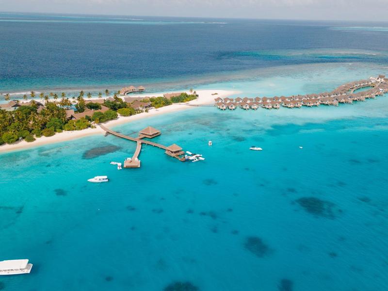 Vista aérea de un resort con bungalows sobre agua clara y playas de arena blanca.