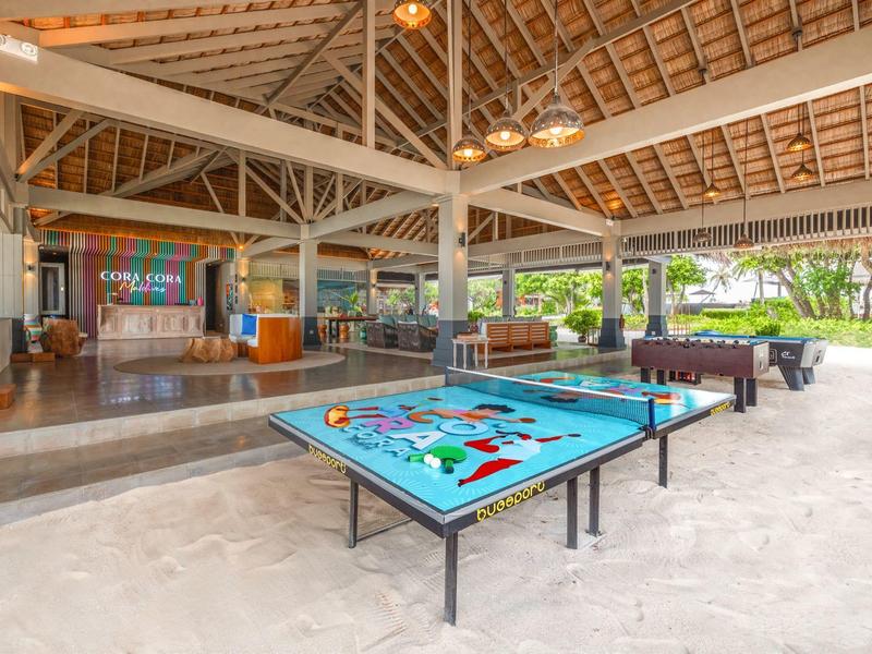 Área de juegos abierta con mesa de billar y futbolín en un hotel tropical con vista al jardín.
