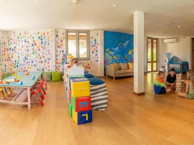 Gran sala de juegos infantil luminosa en hotel con suelo de madera y juguetes coloridos en las paredes.
