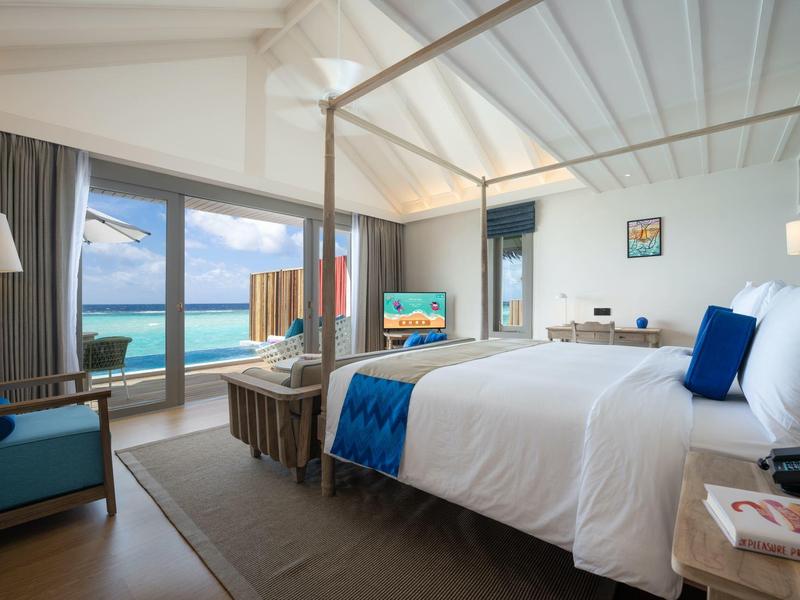 Habitación de hotel luminosa con vistas al mar, cama baldaquín blanca y muebles modernos.