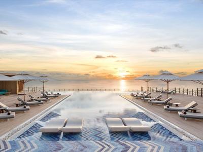 Área de piscina moderna con tumbonas y terraza en la azotea junto al mar al atardecer
