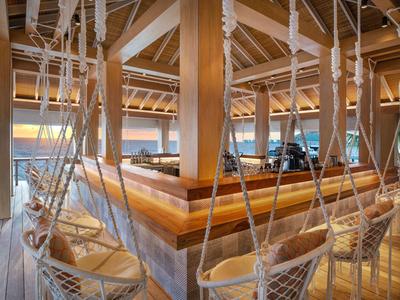 Cómodas sillas colgantes en un lounge abierto con vigas de madera y vista al mar.