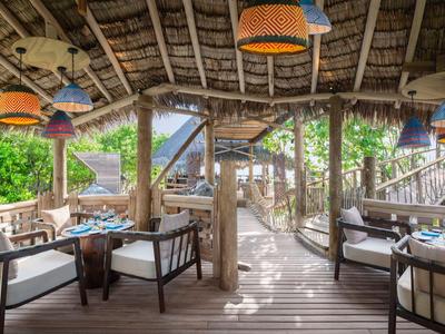 Otwarty drewniany taras z miejscem do siedzenia i kolorowymi lampami w tropikalnym otoczeniu.