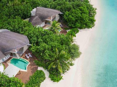 Dos bungalows con piscinas privadas rodeados de vegetación densa en una playa de arena blanca junto a aguas claras y azules.