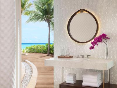 Mueble de baño moderno con toallas, espejo y orquídea, vista a la terraza y al mar.