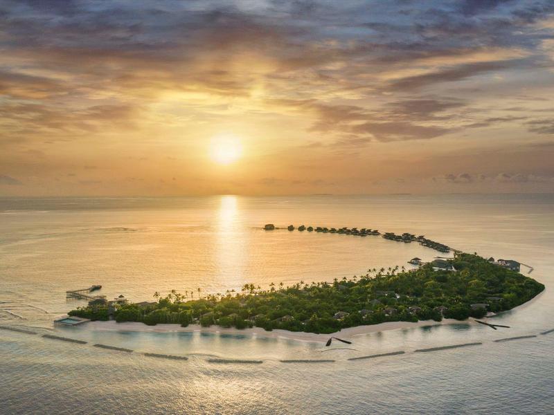 Puesta de sol sobre una isla tropical en el mar con vegetación densa y aguas poco profundas.