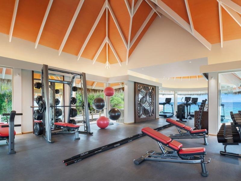 Un gimnasio moderno y luminoso con equipos rojos y negros y grandes ventanas.