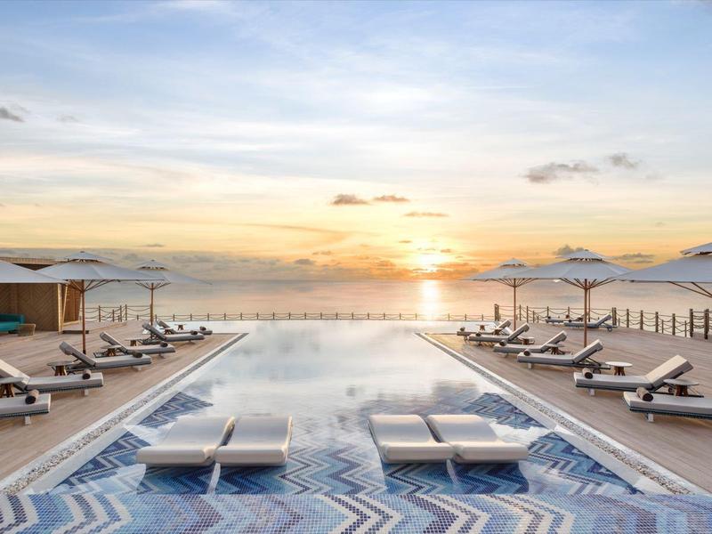 Área de piscina moderna con tumbonas y terraza en la azotea junto al mar al atardecer