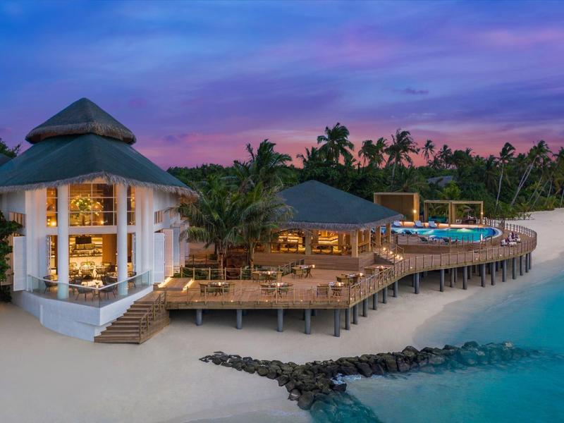 Resort de bungalós de lujo en playa de arena blanca con palmeras y atardecer colorido.