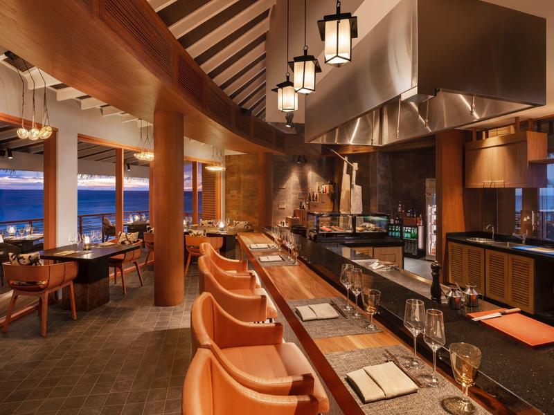 Restaurante moderno y acogedor con barra, luz cálida y vista al mar.
