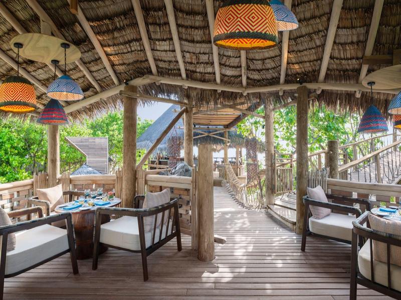 Acogedora terraza con muebles de madera con vistas a un puente en un entorno tropical.
