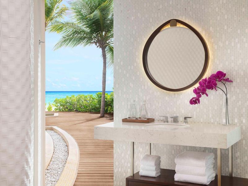 Mueble de baño moderno con toallas, espejo y orquídea, vista a la terraza y al mar.