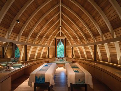 Salle de spa confortable avec deux tables de massage sous un plafond voûté en bois.