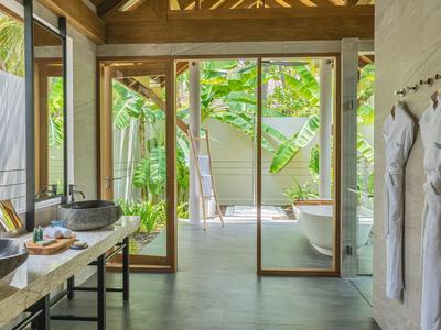 Espace de salle de bain d'hôtel moderne avec lavabo, peignoirs et accès à une terrasse avec chaise longue.