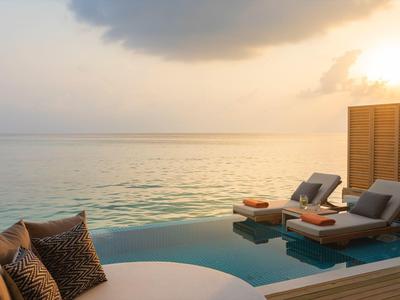 Terrasse luxueuse avec piscine et transats face à la mer calme au coucher du soleil.