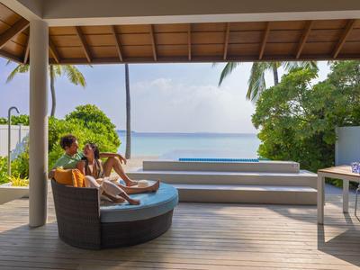 Deux personnes se détendent sur une terrasse avec vue sur la mer et les palmiers.