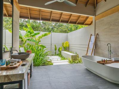 Salle de bain ouverte avec baignoire blanche et jardin extérieur verdoyant.
