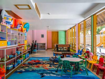 Salle de jeux colorée avec étagères, tables, chaises et jouets pour enfants.