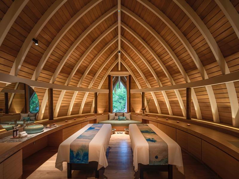 Salle de spa confortable avec deux tables de massage sous un plafond voûté en bois.