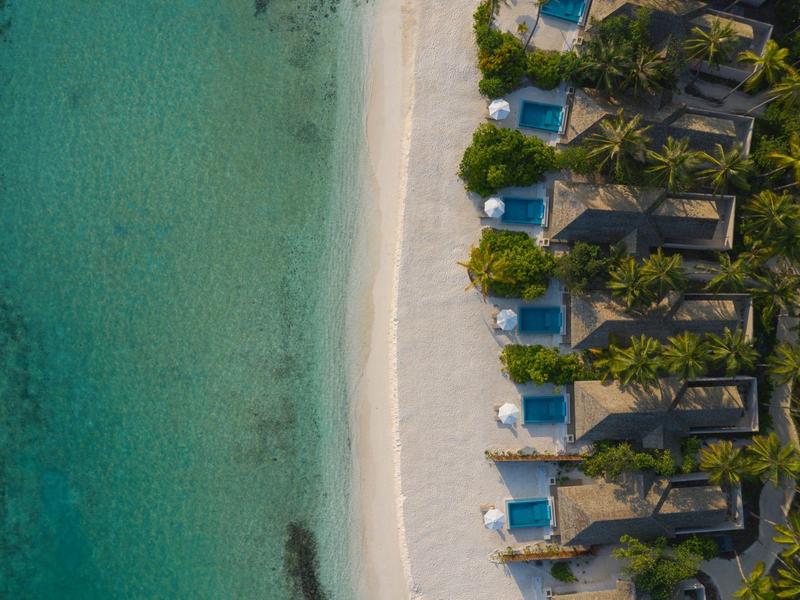 Vue aérienne d'un complexe hôtelier sur la plage avec des hamacs et de l'eau turquoise.
