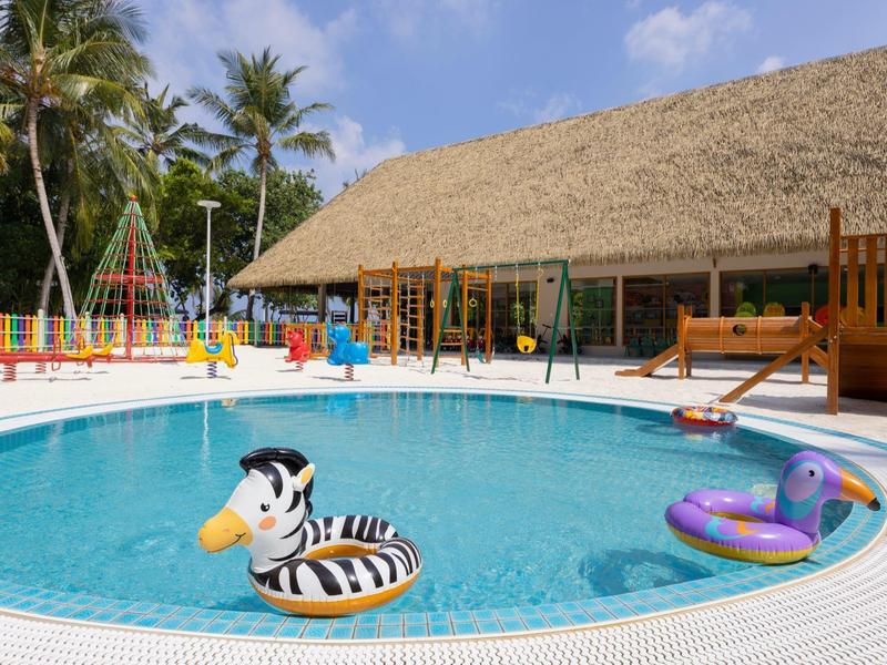 Piscine ronde avec pataugeoire pour enfants, toboggan coloré et toit en chaume en arrière-plan