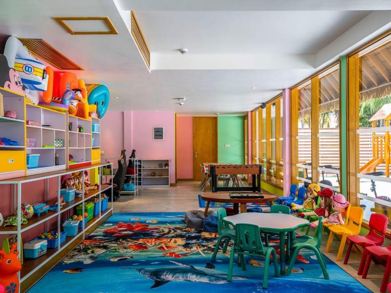 Salle de jeux colorée avec étagères, tables, chaises et jouets pour enfants.