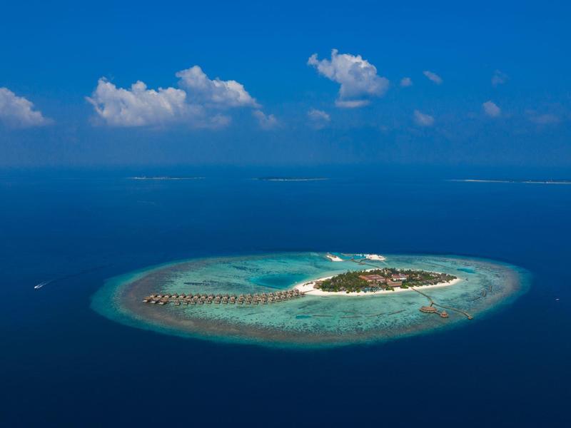 Petite île tropicale avec plage de sable et bungalows sur pilotis dans l'océan bleu clair.