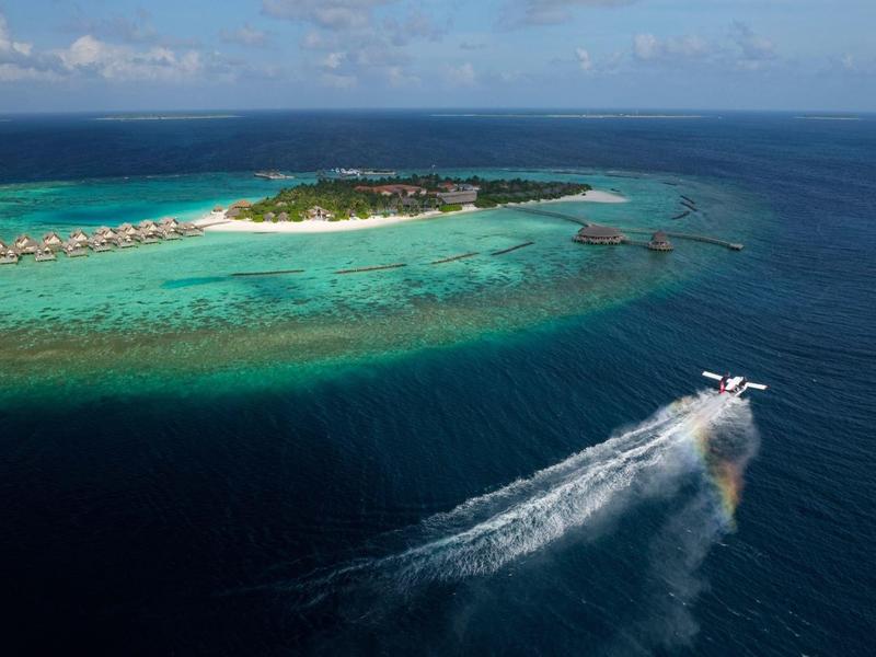 Vue aérienne d'une île avec des bungalows et un bateau sur la mer.