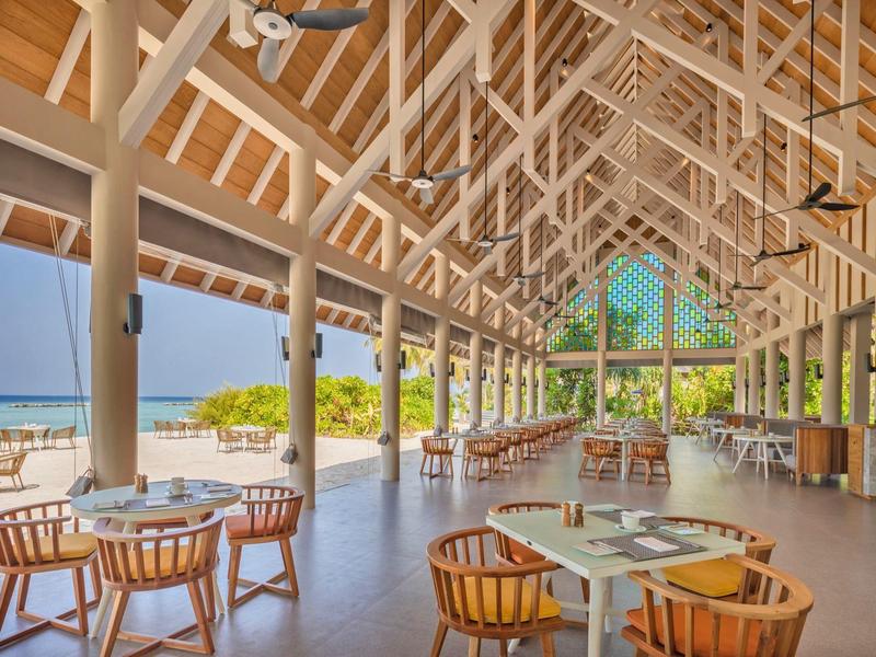 Espace restaurant ouvert avec poutres en bois et vue sur la plage et la mer.