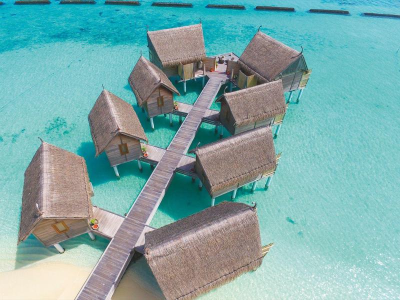 Overwater bungalows connected by wooden walkways in turquoise sea.