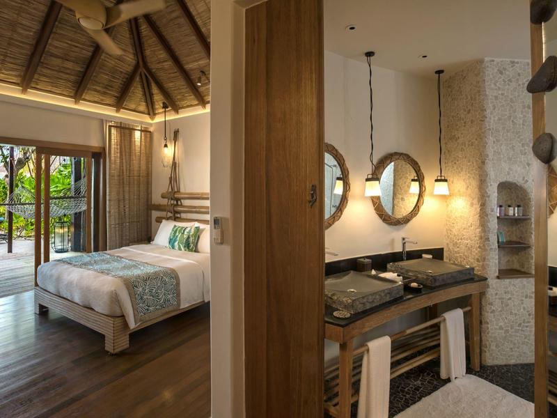 Cozy hotel room with wooden floors, large bed, and open door to tropical garden.