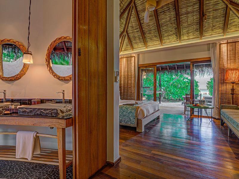 Cozy wooden hotel room with twin beds and bathroom, lush garden view outside the glass door.