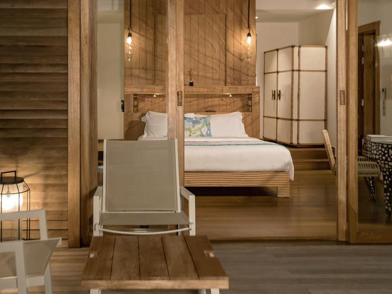 Cozy wooden room with a bed, white chair, table, and warm lighting indoors.