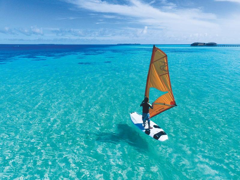 Man windsurfing on clear turquoise ocean under blue sky with clouds