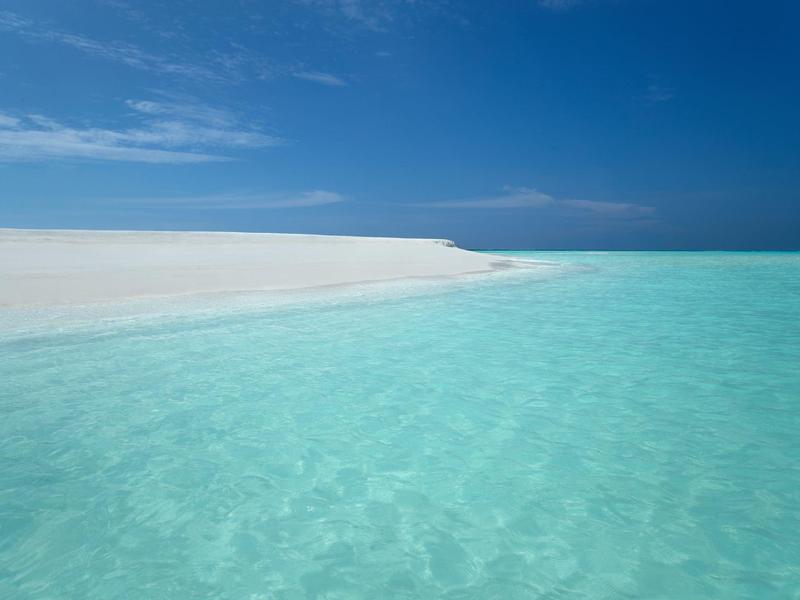 Clear turquoise water meets a white sandy beach under a partly cloudy blue sky.
