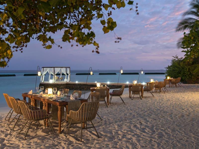 Cozy beachfront dining setup on soft sand with twilight sky and calm sea in background.
