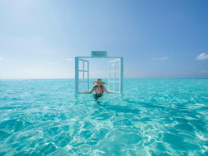 Person enjoying clear turquoise ocean water near an open window frame under a sunny sky.