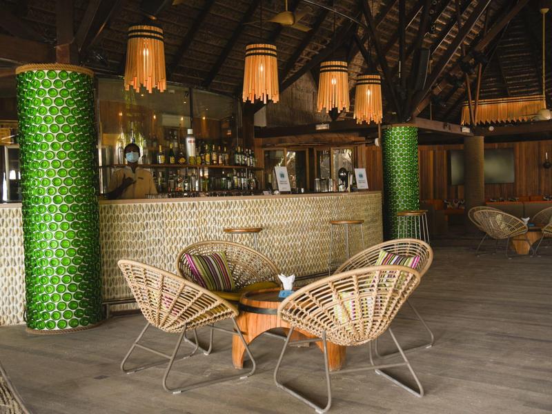 Cozy bar area with wicker chairs, wooden flooring, and hanging lamps under a thatched roof.