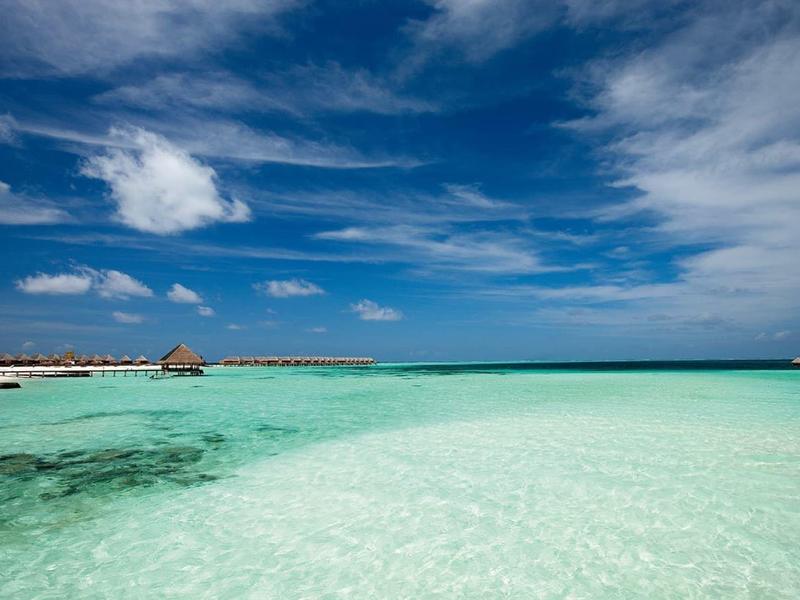 Clear turquoise water with overwater bungalows under a blue sky with clouds.