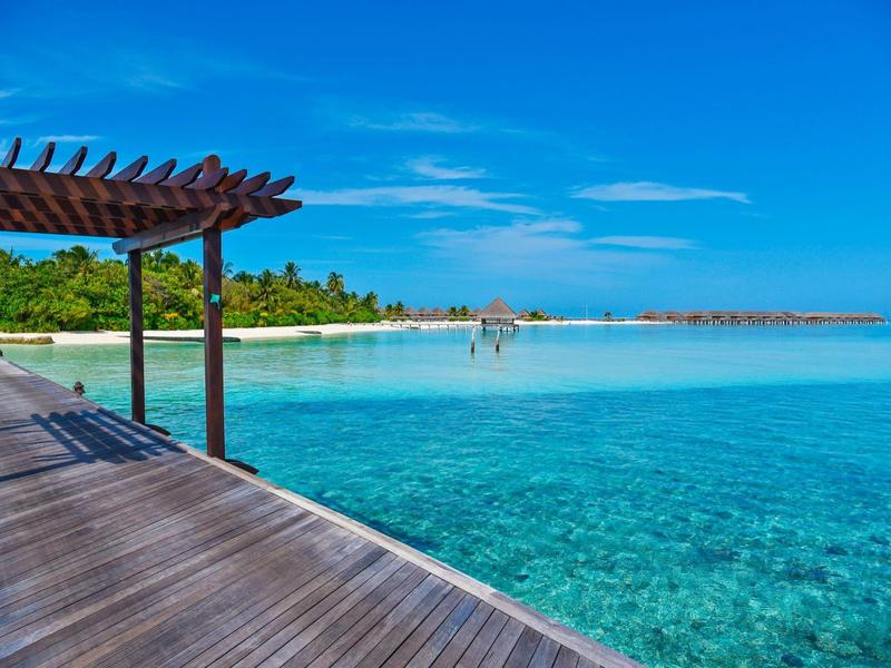 Clear blue sea with wooden pier and pergola under a sunny sky at a tropical beach.