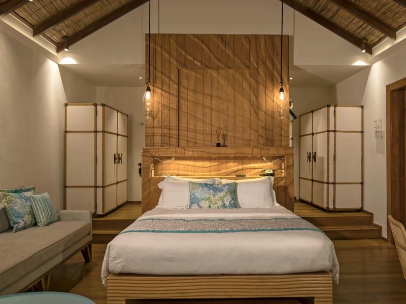 Cozy hotel room with large bed, wooden furniture, and warm lighting under a thatched roof.