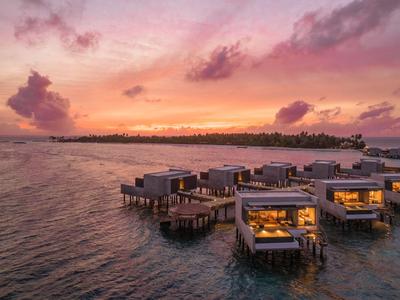 Overwater bungalows at sunset over clear water with colorful sky.