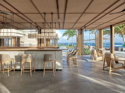 Nowoczesna, otwarta kawiarnia z hokerami i miejscami do siedzenia z widokiem na morze i palmy.