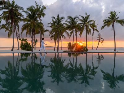 A pool with palm trees and sunset in the background at a tropical vacation spot.