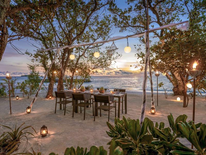 Kolacja na plaży pod lampkami z widokiem na zachód słońca nad morzem.