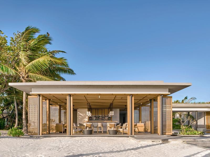 Nowoczesny otwarty dom na plaży z drewnianą konstrukcją, dużymi szklanymi oknami i palmami w tle.