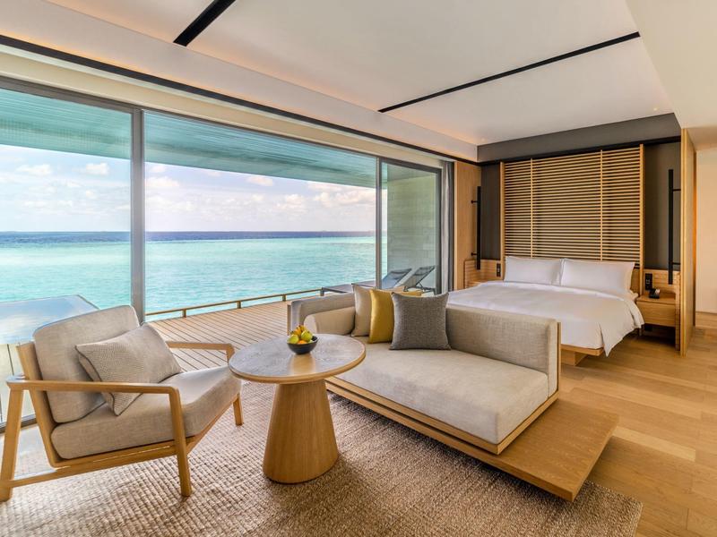 Nowoczesny pokój hotelowy z dużym panoramicznym oknem i widokiem na morze, wygodnym miejscem do siedzenia i łóżkiem.