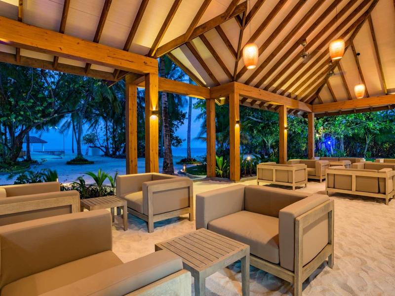 Outdoor lounge with modern seating and view of tropical plants at dusk.