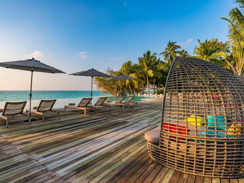 Beach area with loungers, umbrellas, and a cozy wicker chair overlooking tropical sea.